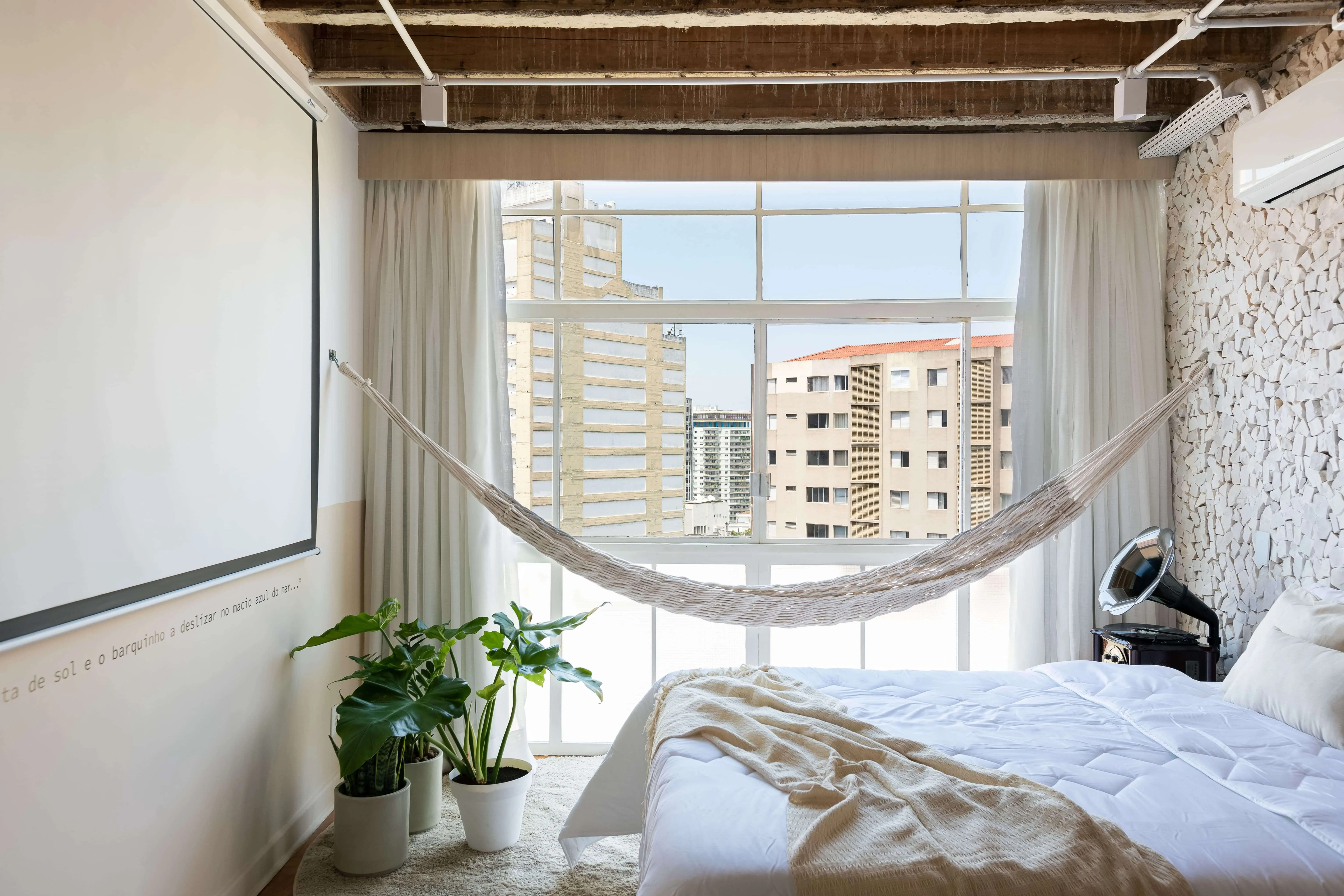 Cama queen, rede na janela e tela de projeção, criando um ambiente relaxante.