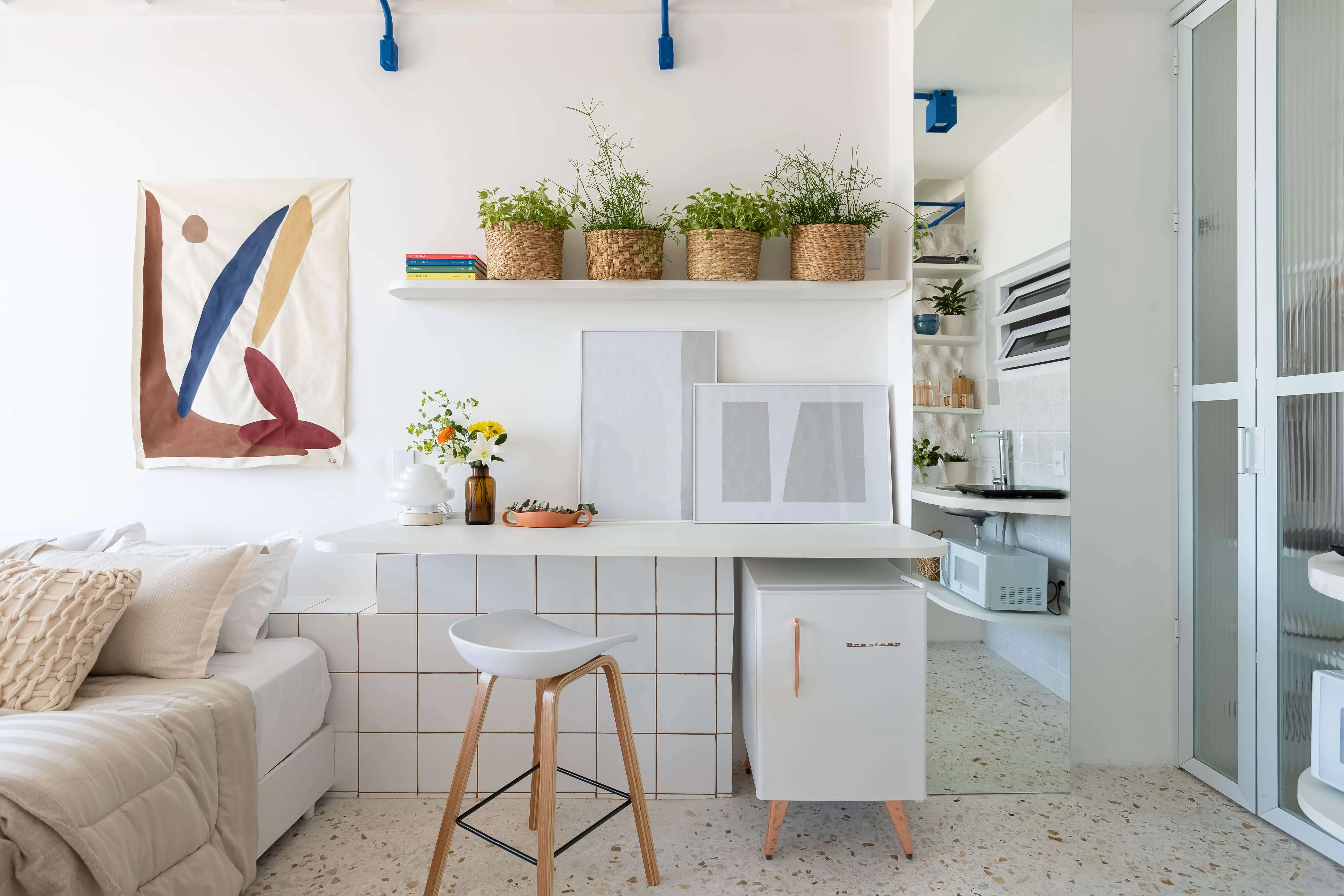 Frigobar, plantas e quadro ao lado da cama.